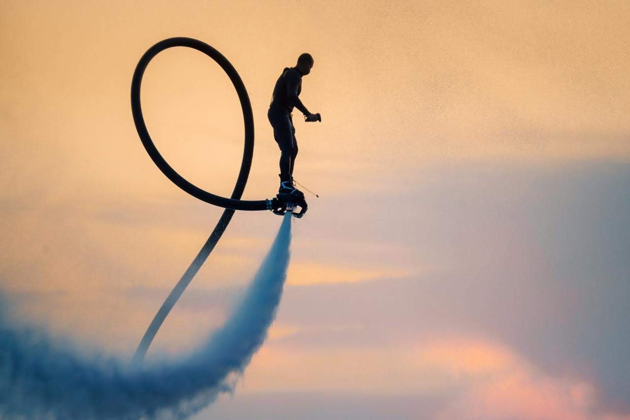 Silhouette of a flyboard rider looping a hose at sunset over the water in Phuket